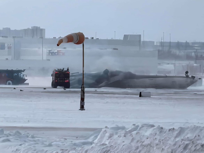 Delta Airlines plane upside down after crash landing, surrounded by snow and emergency vehicles.