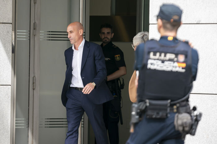 Former football head leaving a building, surrounded by police officers, after being fined €10,000.