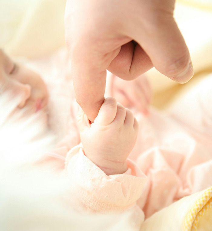 Baby holding an adult’s finger, representing Generation Beta connection.