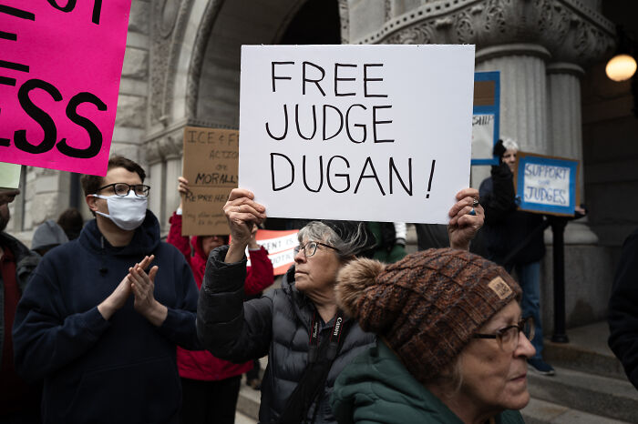 Protesters holding signs outside courthouse supporting judge suspended amid ICE defendant evasion allegations.