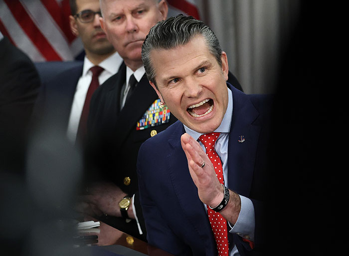 Man in a suit passionately speaking at a meeting, related to Trump and war plans.