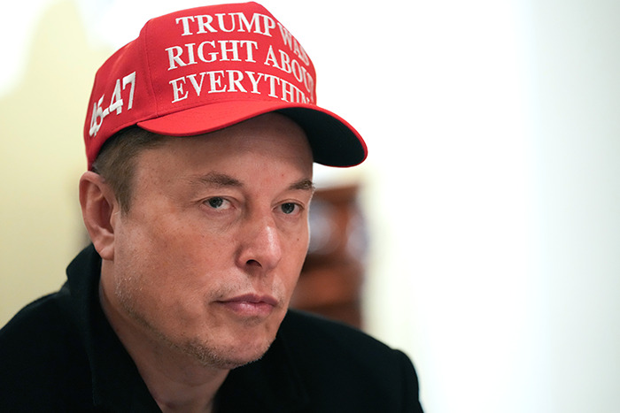 Person wearing a red cap with a message about Trump, in a serious setting.