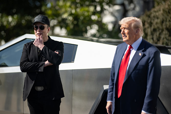 Man in black by a Tesla vehicle, with another man in suit, highlighting Tesla's first quarter earnings concerns.