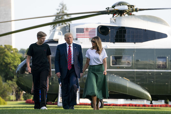 Melania Trump with Donald Trump and Barron walking on grass near helicopter amid rumors about Barron’s college hunt.
