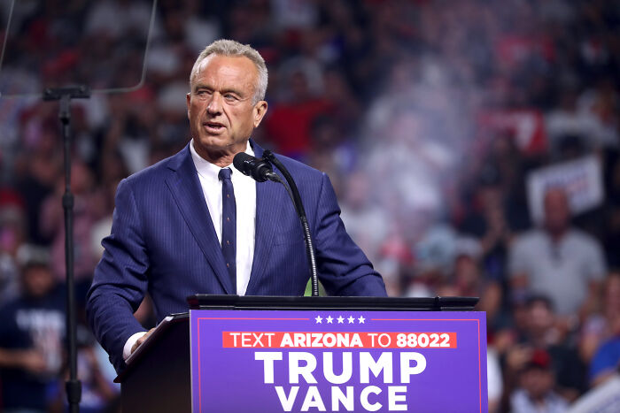 Speaker at podium during a crowded event, related to Health Secretary RFK Jr. swimming with grandkids in sewage-filled creek. Speaker at podium during a crowded event, related to Health Secretary RFK Jr. swimming with grandkids in sewage-filled creek.