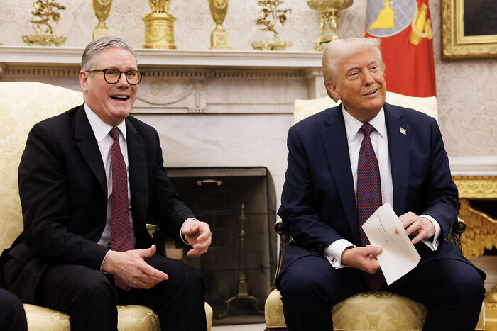 Two men in suits seated in a formal room, highlighting Trump’s tariff strategy while China quietly wins global trade.