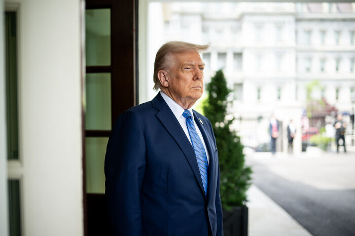 A man in a suit stands near a doorway with a serious expression amid Biden cancer diagnosis conspiracy theories.