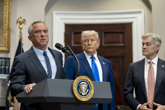 Man speaking at presidential podium with two suited men behind him, related to RFK Jr. medical advice remarks.