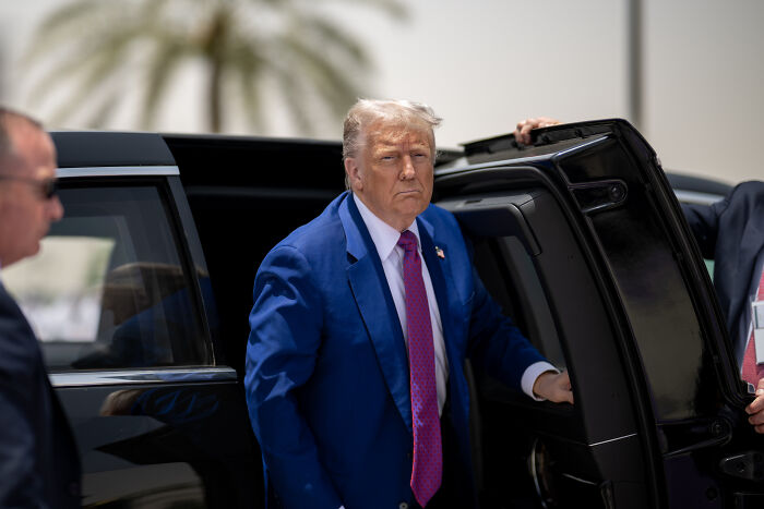 Former president in a blue suit exiting a black vehicle, related to sheriff bribery and law enforcement badges controversy.