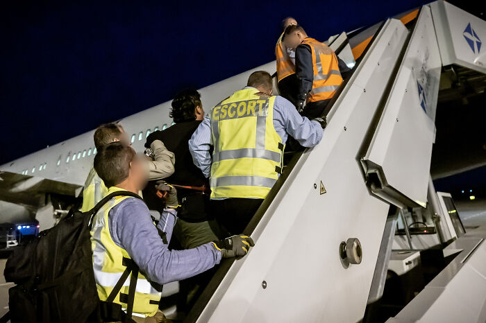 Officials escort Asian migrants boarding a plane amid U.S. deportations to African country on brink of civil war.