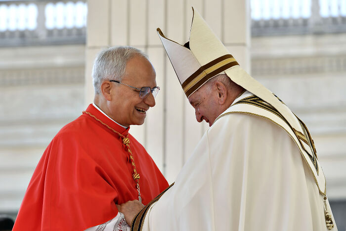 New Pope Leo XIV in white robes and mitre greeting a cardinal in red, amid child abuse claims at former Chicago parish.