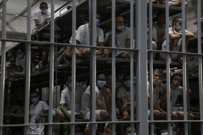 Migrants wearing masks crowded inside a Texas detention facility visible through metal bars in dim lighting.