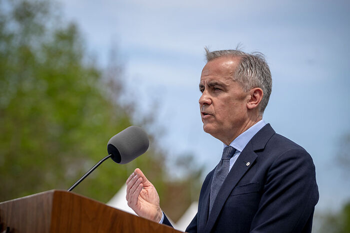 Man in a suit speaking outdoors at a podium about bold defense deal and Canada joining the US as 51st state.