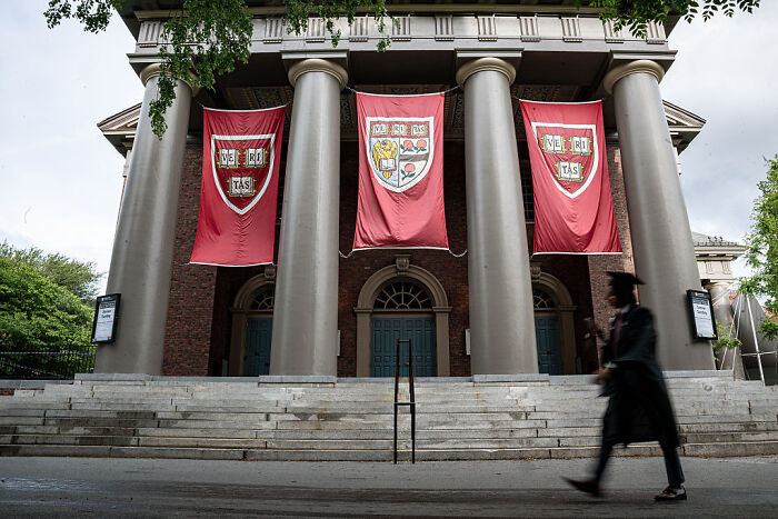 Harvard University building with banners and a person in graduation attire walking by, related to Barron’s college hunt.