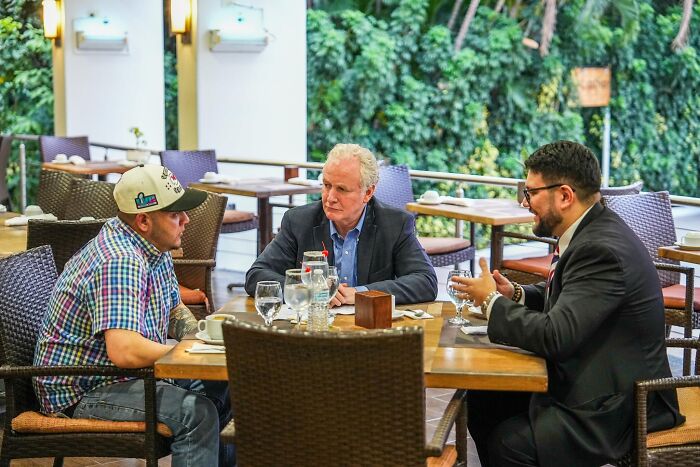 Three men including Rubio and Van Hollen in a heated discussion over deportees at an outdoor restaurant setting.