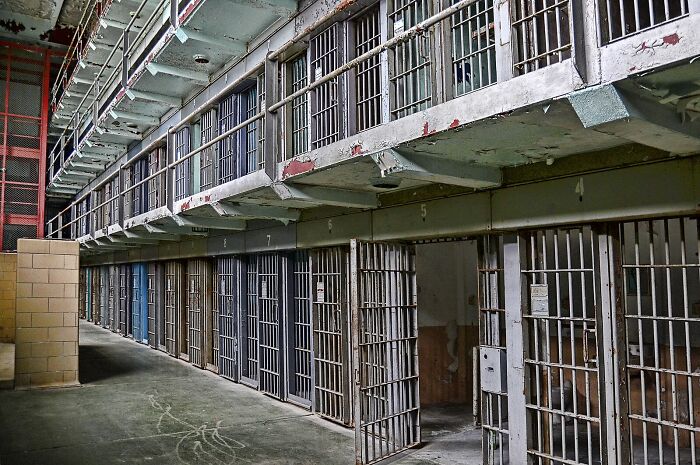 Interior view of a private prison with metal barred cells highlighting Trump’s private prison pals and migrant crackdowns.