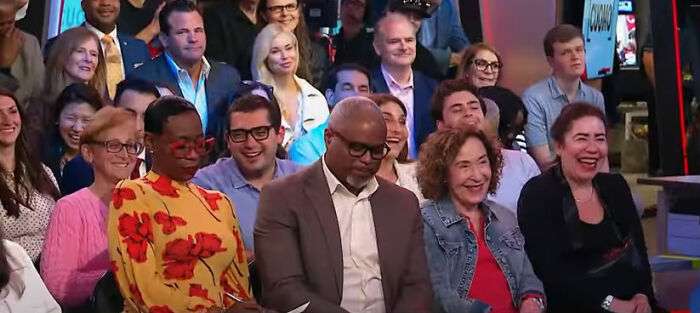 Audience members at a town hall event reacting with laughter during a discussion about Trump’s first 100 days.
