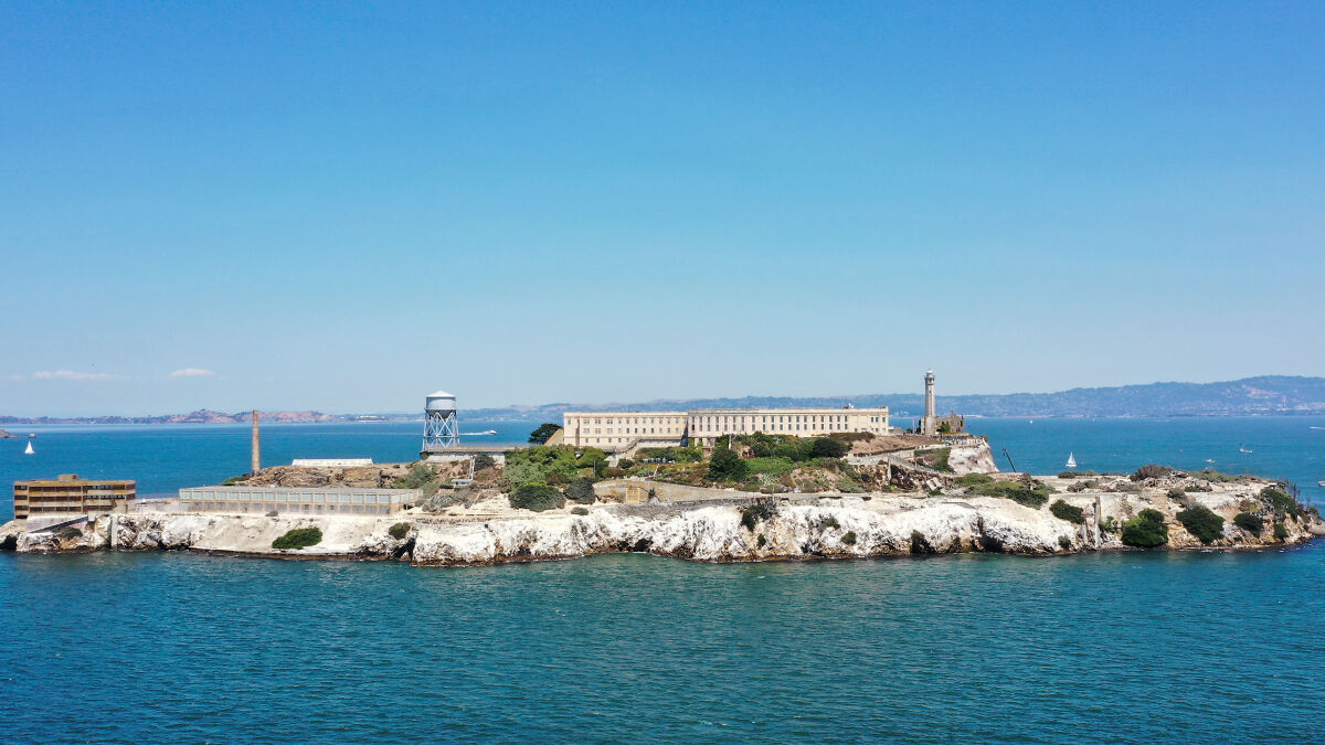 Aerial view of Alcatraz Prison island in San Francisco Bay with clear skies and surrounding blue water.
