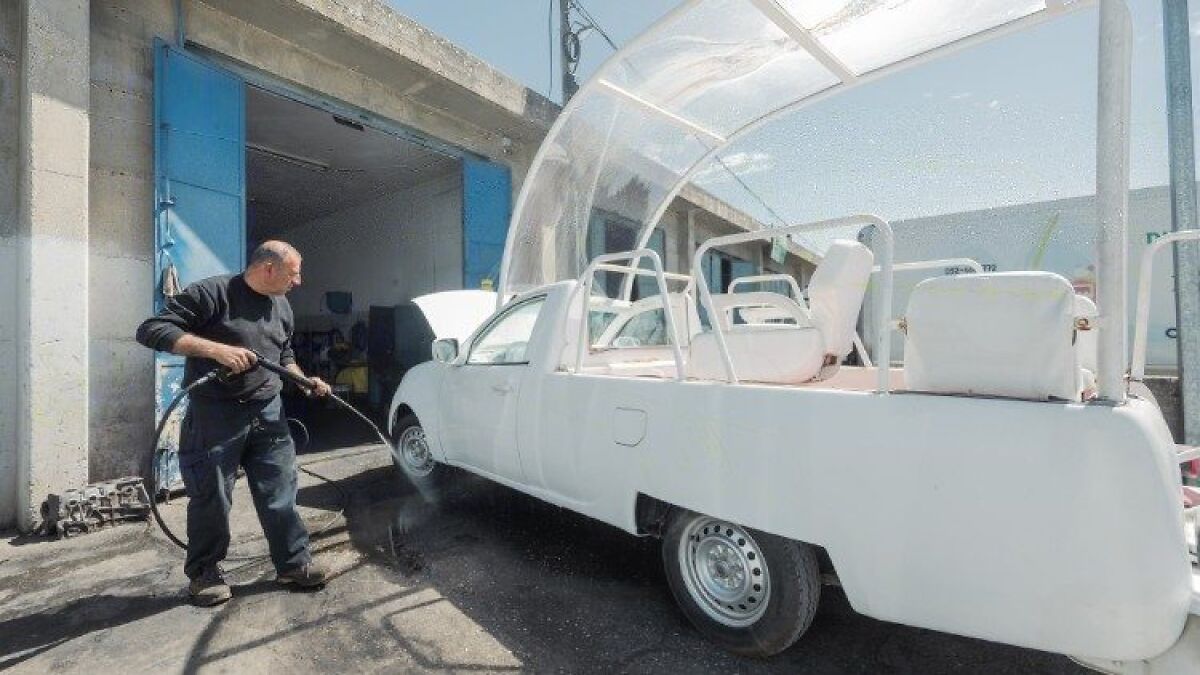 Man cleaning white Popemobile vehicle being converted into mobile health unit for Gaza children outside garage on a sunny day