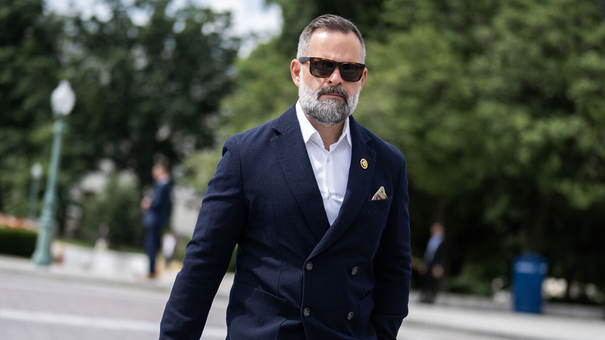 Man wearing sunglasses and a navy blazer, walking outside, linked to Republican accused of lying about military service and Bronze Star.
