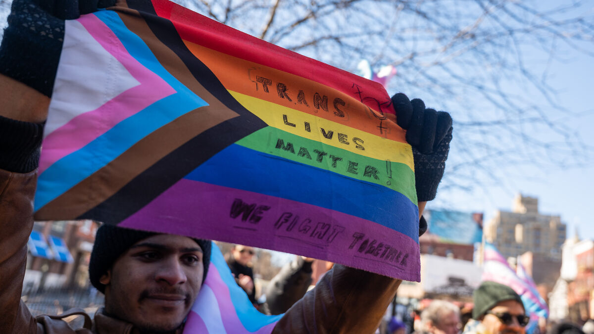 Protester holding a trans pride flag with Trans Lives Matter, amid court decision on trans troops policy.