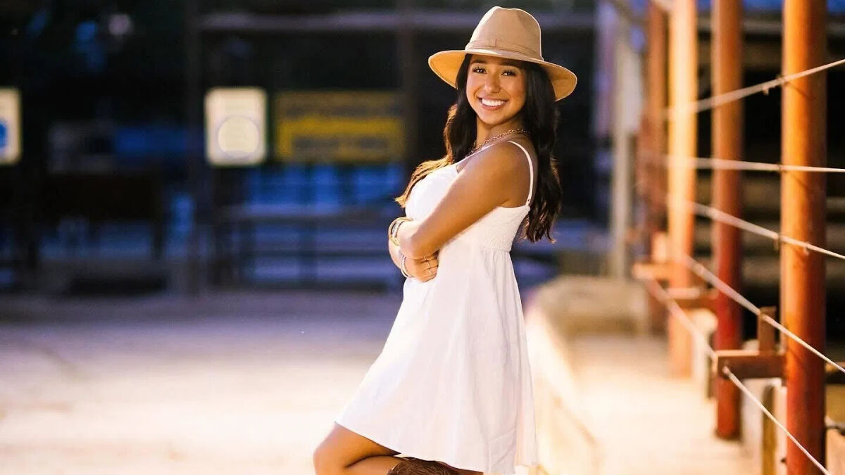Young college student wearing a white dress and hat, smiling while standing outdoors, related to deportation and illegal turn keywords.