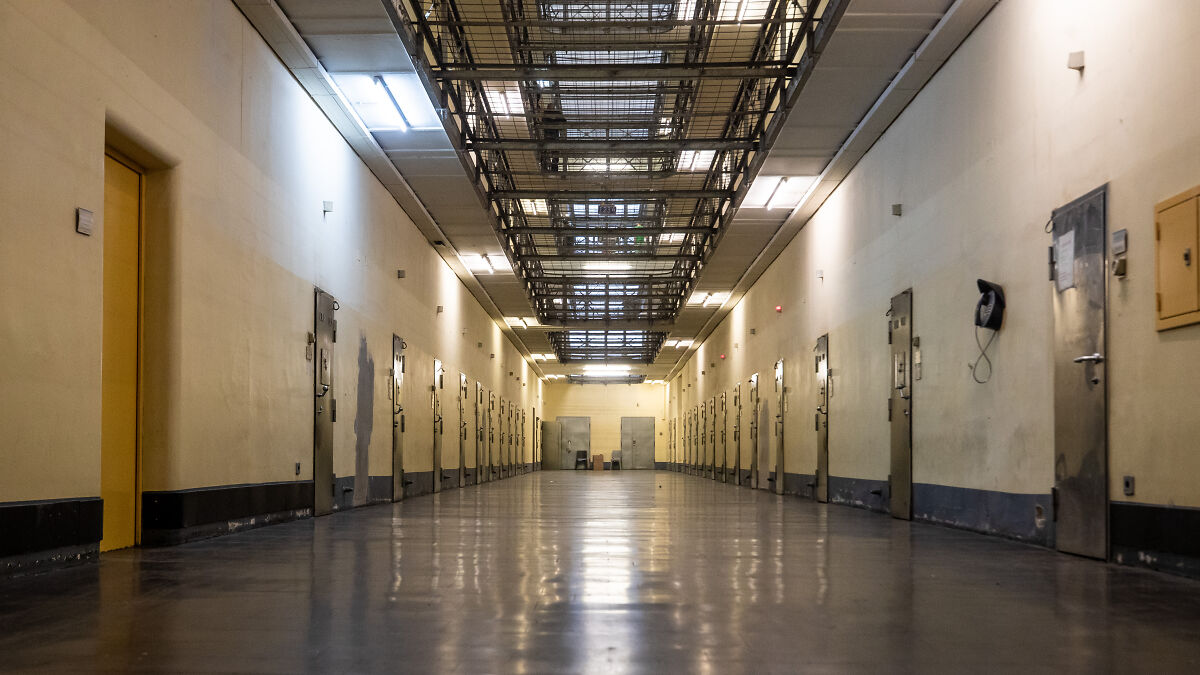 Empty prison corridor with metal doors on both sides symbolizing orphanage abuse and harsh childhood memories