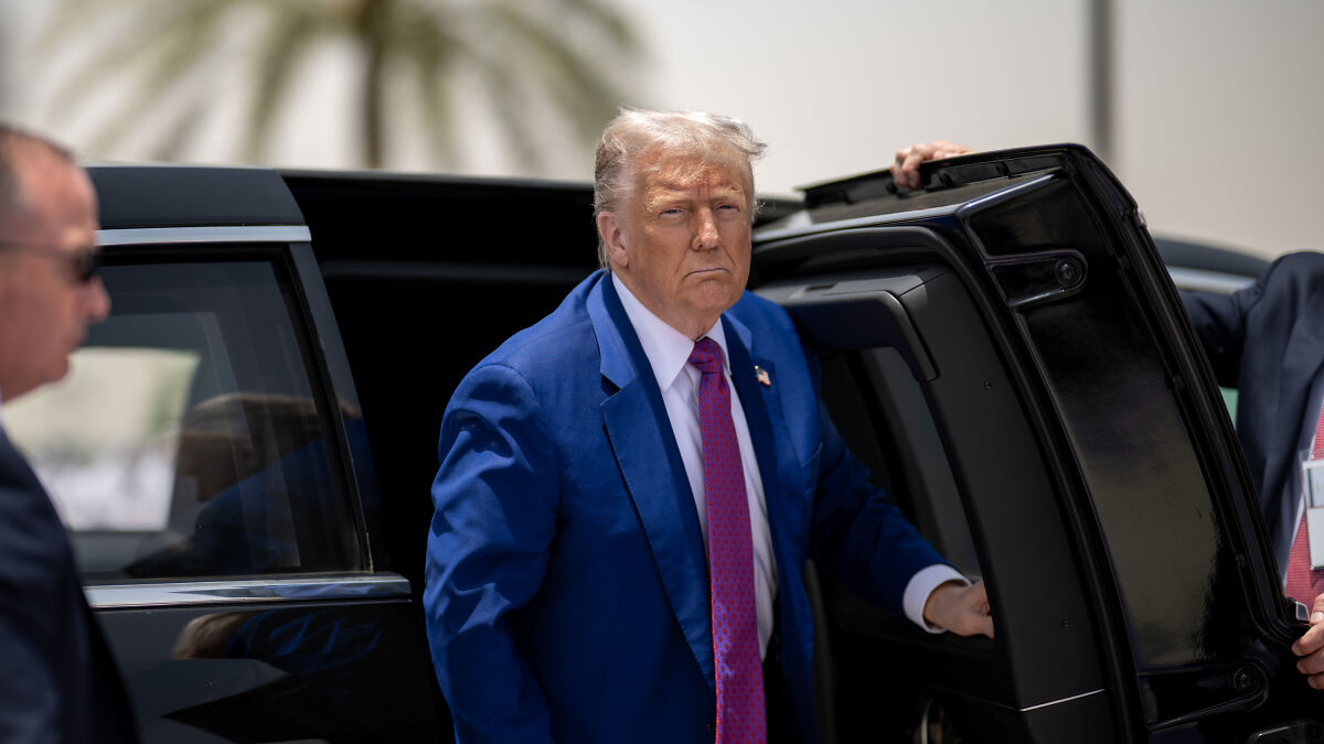 Man in blue suit and red tie stepping out of black car, symbolizing sheriff bribery and law enforcement badge controversy.