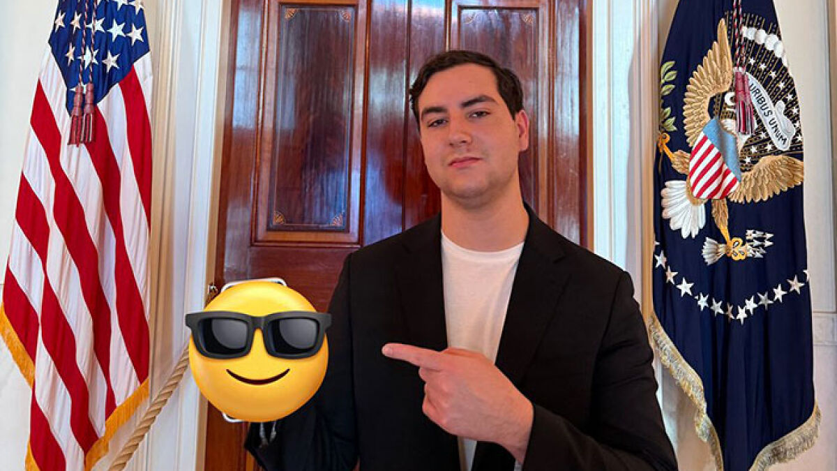 Young man posing in front of US flags, representing crypto bros at a Trump event criticized for the dinner they received
