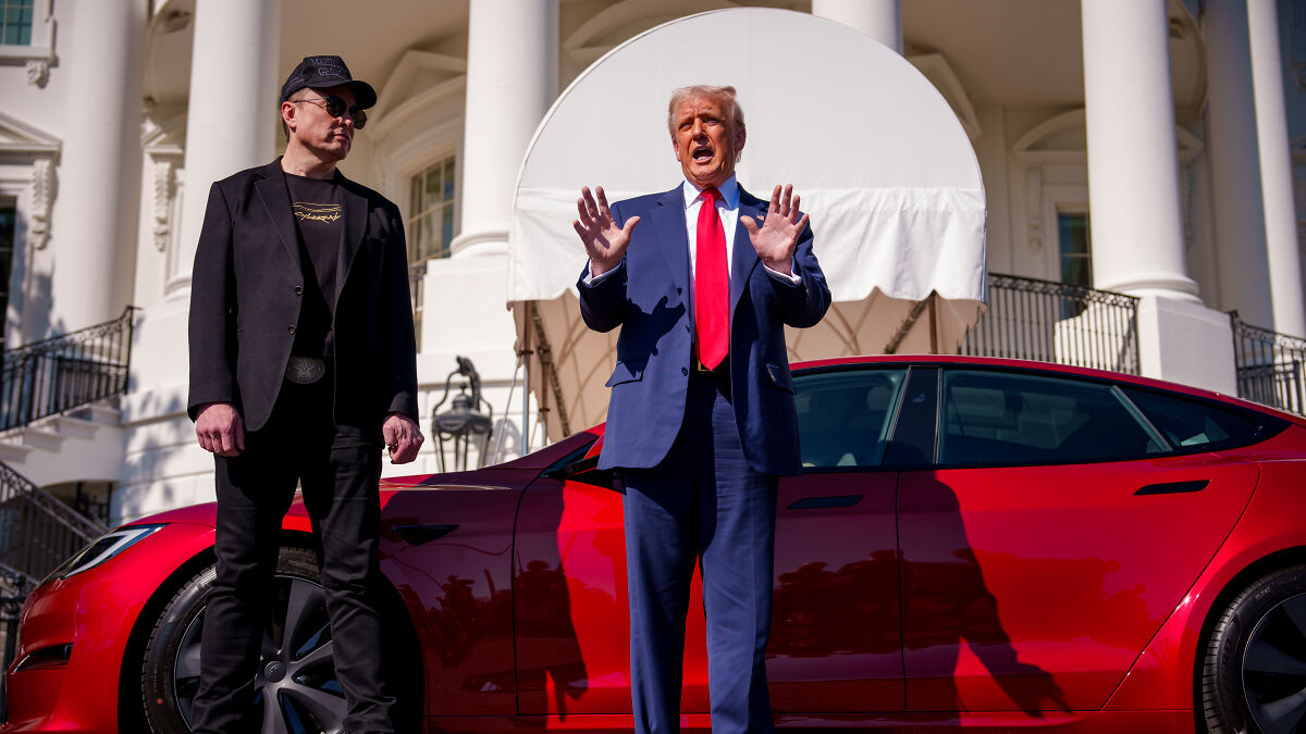 Elon Musk standing beside red Tesla car with man in suit discussing government waste outside White House.