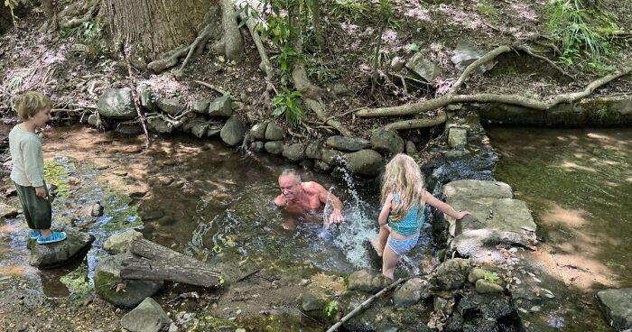 Health Secretary RFK Jr. swimming with grandkids in a creek flowing with sewage and bacteria surrounded by trees and rocks.
