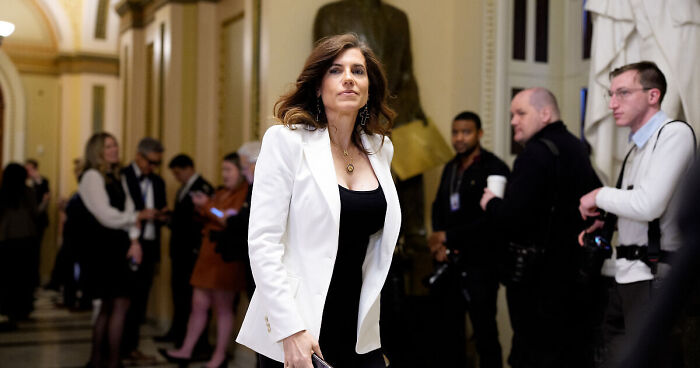 Nancy Mace walking confidently in a hallway during a House hearing surrounded by people and photographers.