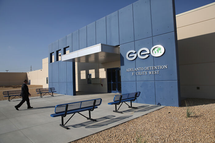 Exterior of a GEO private prison facility with benches outside under clear sky linked to Trump’s private prison pals and migrant crackdowns.