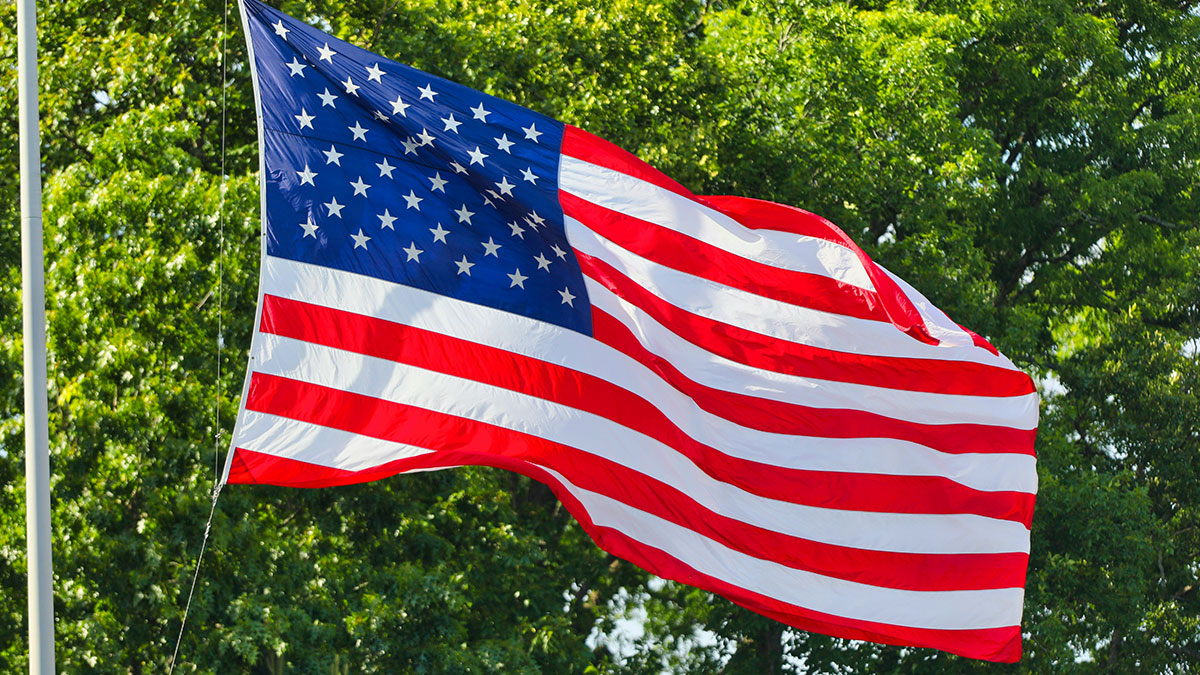 American flag waving outdoors in front of green trees representing U.S. and China tariff deal discussions.
