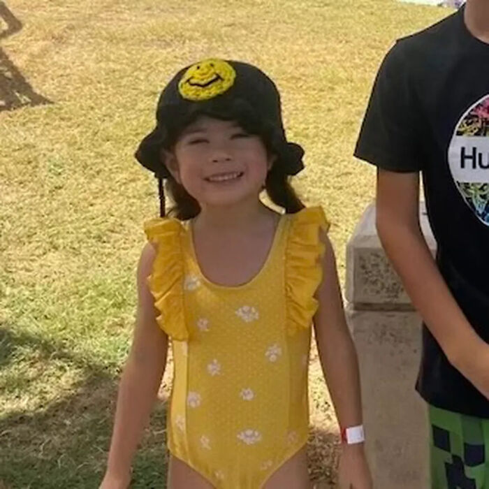 Young girl smiling outdoors wearing yellow swimsuit and black hat, related to fatal shooting involving brother and dad’s rifle at home.