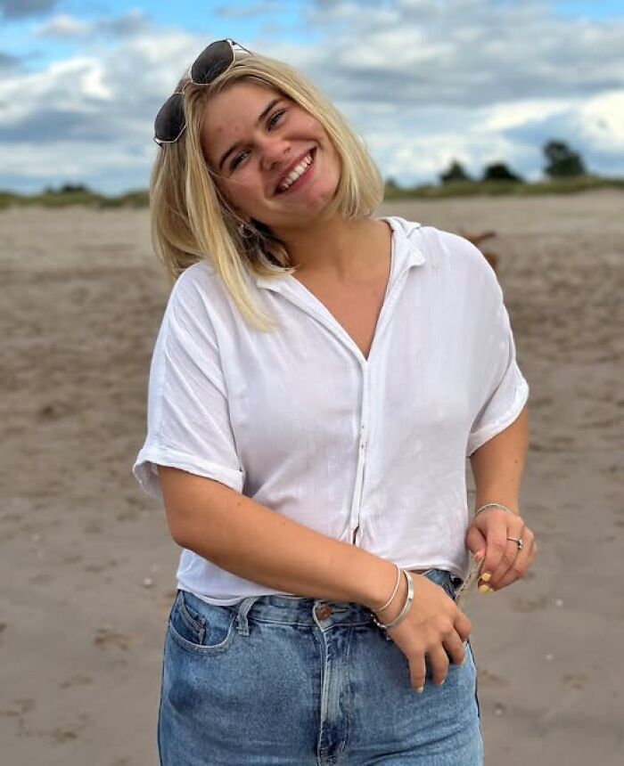 Young woman smiling on a beach with sunglasses on her head, unrelated to man accessed porn 170 times case.