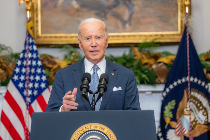 President Biden speaking at a podium with US flags in background amid probe into autopen use in West Wing power.