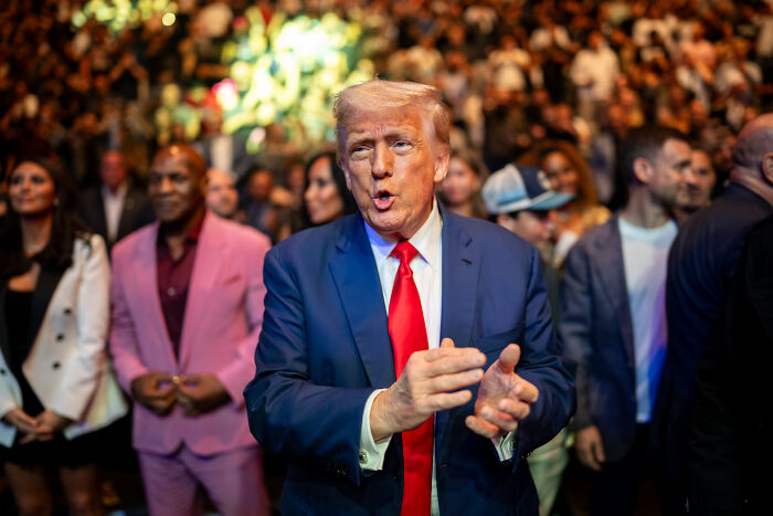 Man in a blue suit and red tie clapping at a crowded event, highlighting MAGA’s hypocrisy in viral Obama video.