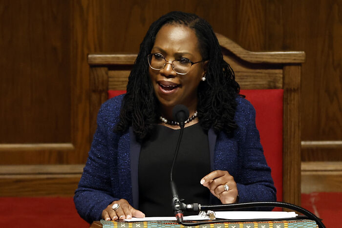 Woman speaking at a wooden podium with a microphone, related to Supreme Court and reverse discrimination case discussion.