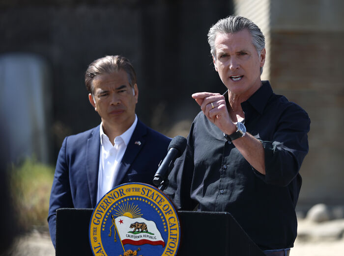 Governor speaking at a press conference about National Guard control amid protests, with another official listening nearby.