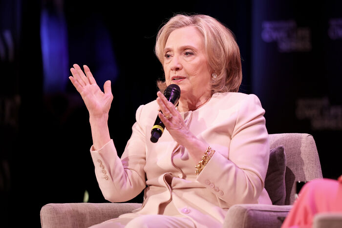 Hillary Clinton speaking into a microphone, discussing politics and criticizing Trump’s low-energy birthday parade.