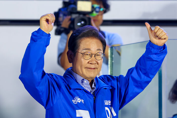 Man in blue jacket raising both fists, representing South Korea, in a moment related to Karoline Leavitt’s viral South Korea question.