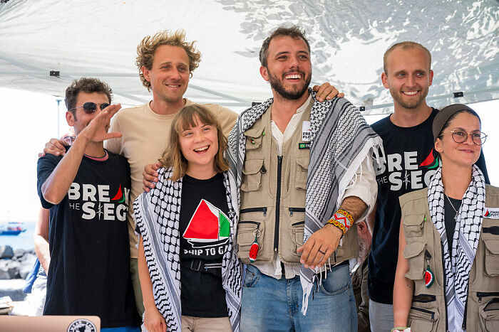 Group of activists wearing freedom flotilla shirts and keffiyeh scarves preparing for Gaza-bound mission event.