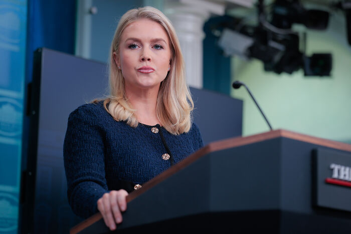 Karoline Leavitt speaking at a podium during a press briefing, capturing her cringe binder shuffle moment on South Korea question.