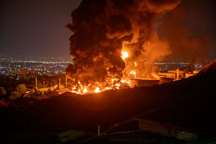 Massive fire and smoke billowing after Israeli missile hits Iran state TV building at night with city lights in background.