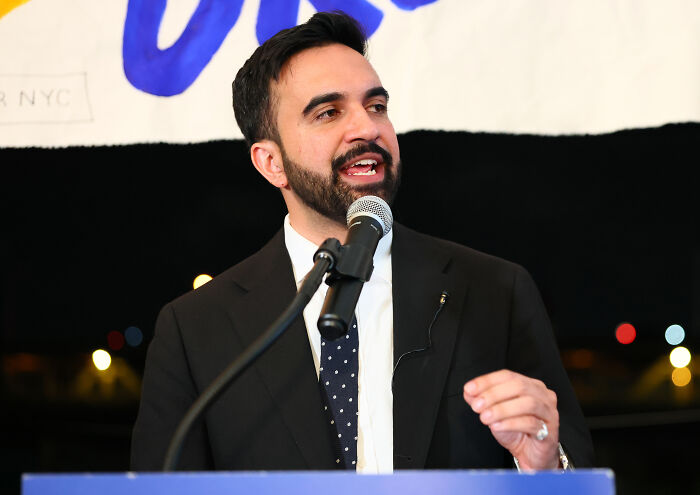 NYC mayoral candidate Zohran Mamdani speaks at a podium, addressing the crowd about New York tax plans.
