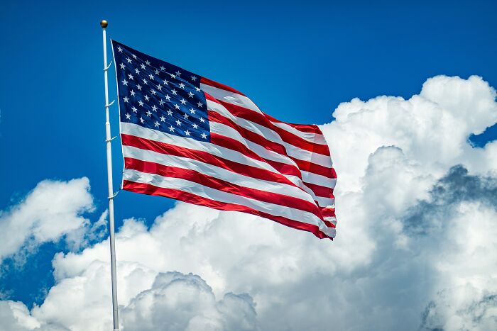 US flag waving against a blue sky symbolizing Trump's travel ban restricting entry from 19 countries to the US.