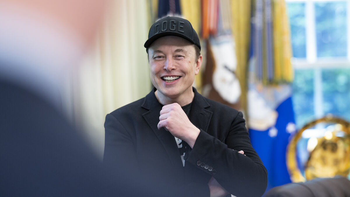 Elon Musk smiling and wearing a black Doge cap in an office, linked to foreign student ban and spaceship topics.