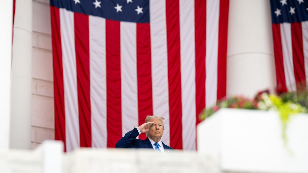 Former President Trump saluting in front of a large American flag during a travel ban announcement event.