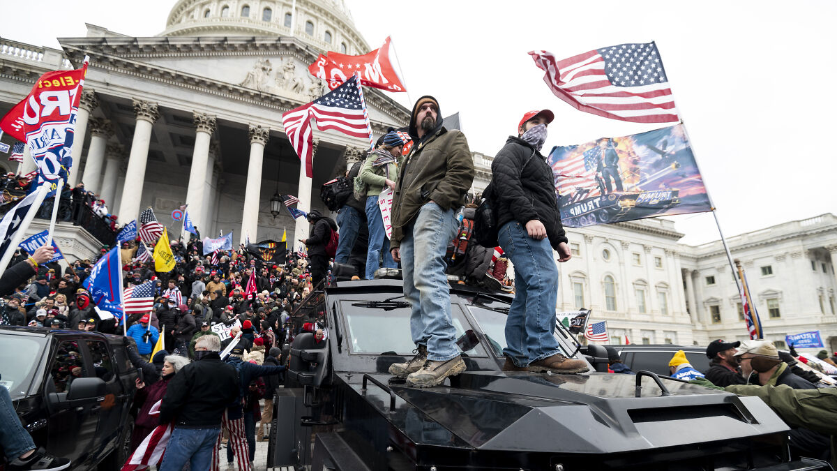 Supporters at the Capitol building during the January 6 riot, many holding American flags and pro-Trump banners.